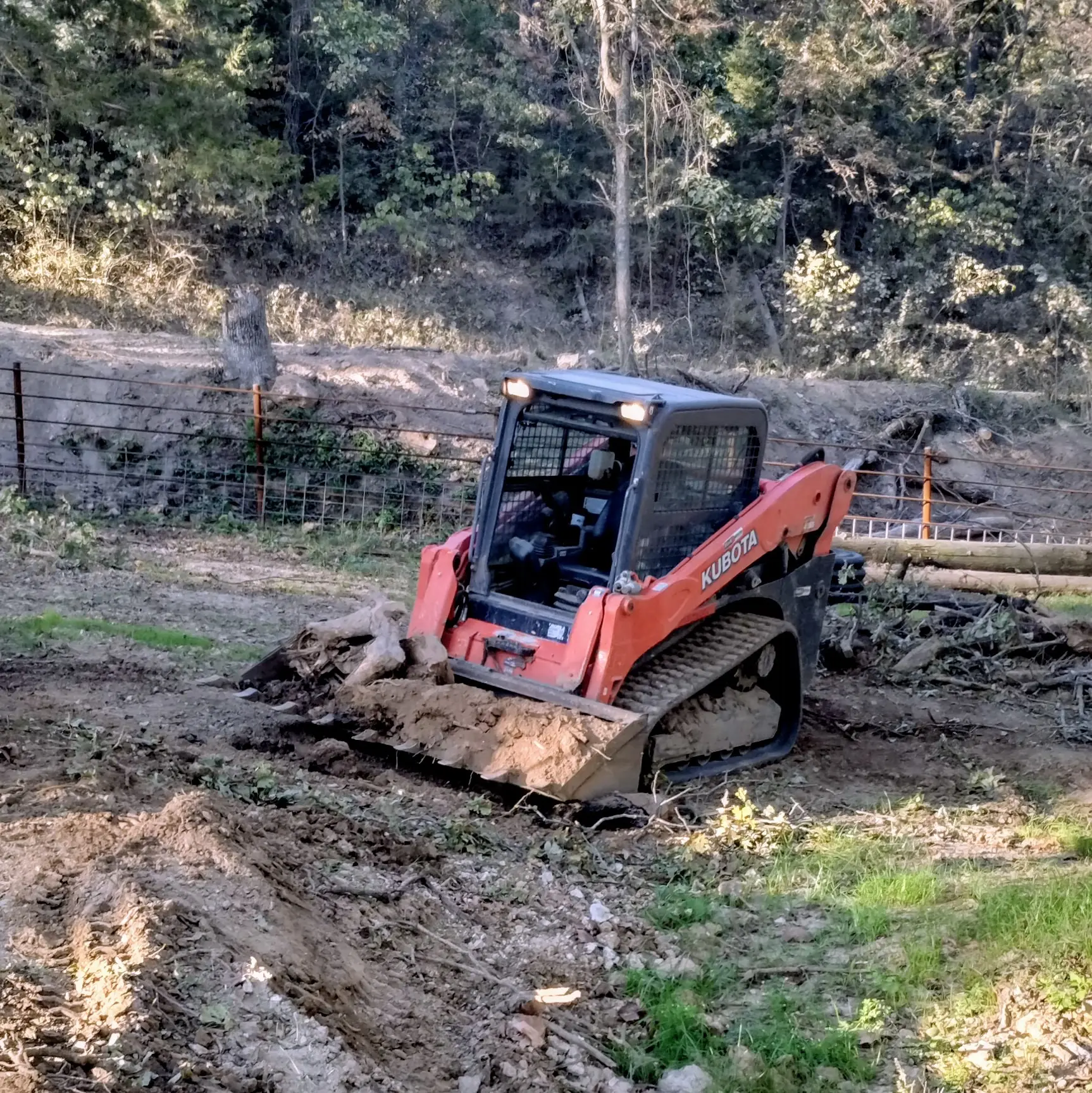 Skid steer loader moving dirt in a wooded area.